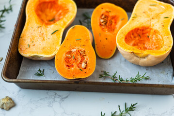 Seasoned butternut squash halves on baking tray with herbs.