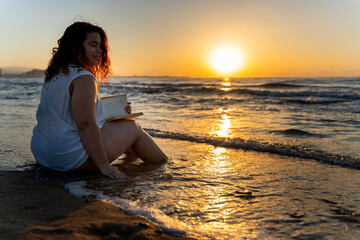 Plus size woman enjoying reading a book on the beach at sunrise
