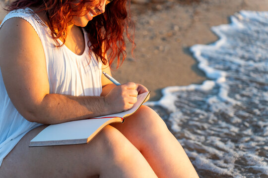 Curvy woman writing on notebook at sunrise beach