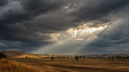 Dramatic sunbeams pierce a dark sky above a rural landscape