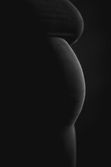 Pregnant belly silhouette on black background – minimal low-key maternity concept with copy space