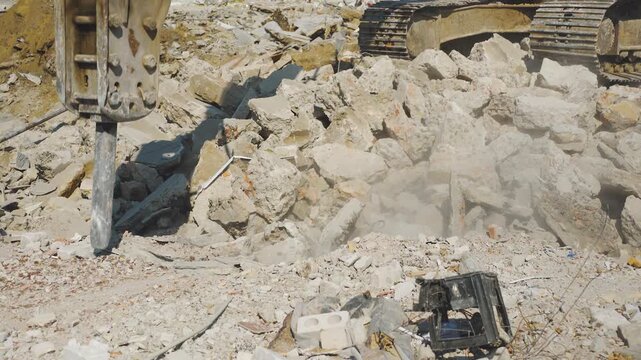Construction excavator working with industrial jackhammer splits blocks of concrete, brick. Process of dismantling, demolished, destroyed house close-up. Hydraulic hammer of crushing machine.