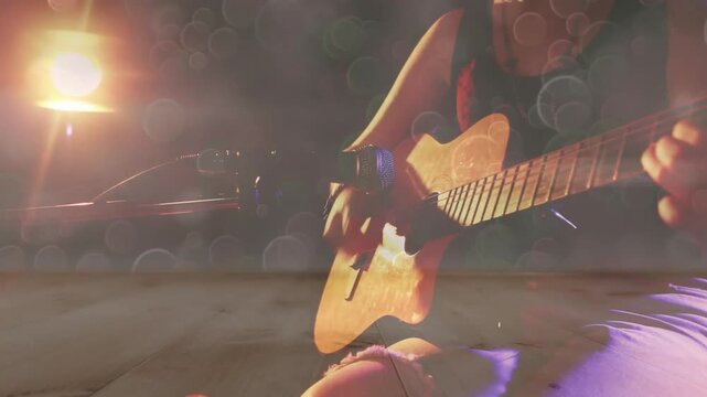 Teenage guitarist bringing acoustic guitar into frame, performing tune under warm spotlight flares