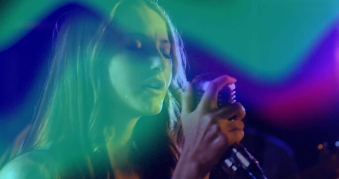 Singer lifting mic and singing for live show with guitarist strumming electric guitar under lights