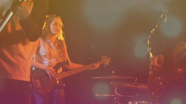 Bearded guitarist strumming guitar under lights sparking bassist, singer harmonizing for music show