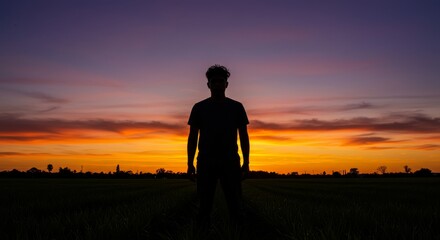 Sunset Silhouette of a Migrant Worker - A silhouette of a man stands in a field at sunset, symbolizing hope, resilience, journey, new beginnings, and perseverance
