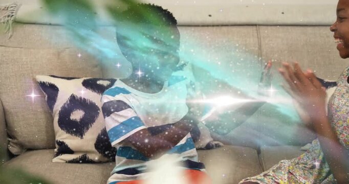 Boy raising hands inviting sister into educational hand-clapping game on sofa, adding sparkle glow
