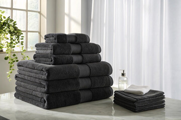 Dark charcoal gray towel set arranged in neat pyramid stack on marble counter with small washcloths...