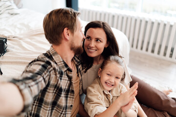 Obraz premium Happy family smiles while father takes selfie, daughter clapping hands joyfully, mother looking lovingly, tender moment filled with fun, warmth, and connection.