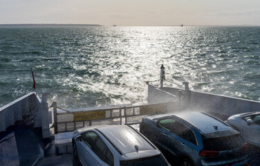 Windy sea spray drenches the vehicles on car ferry traveling from Portsmouth to Fishbourne as it...