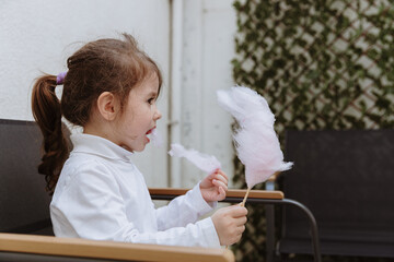 A little girl eats cotton candy on a stick in the garden.