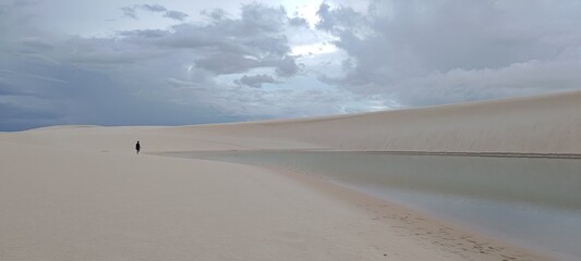 Lençóis Maranhenses, Santo Amaro. A solitary person walks through a desert of white sand dunes next to a natural lagoon. This immense landscape evokes feelings of solitude, freedom, and exploration.
