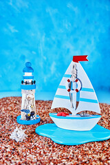 image with miniatures of sailboat, lighthouse, sand and shell on blue background, concept of summer vacation