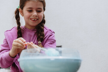 Happy girl with braids makes cotton candy herself in the garden.