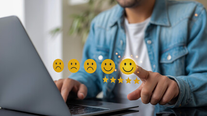 Person's finger touching a happy face emoji and stars on a screen above a laptop customer service feedback