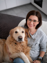 Happy Woman Hugging Adorable Golden Retriever At Home As It Looks Into The Camera