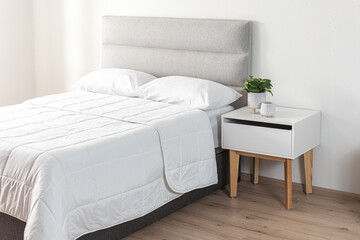 Bright bedroom with textured light gray upholstered headboard, crisp white bedding and modern white nightstand with natural wood legs, styled with minimalist decor and soft morning sunlight ambiance.