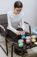 A teenage girl pours blue sugar from a bag into a jar.