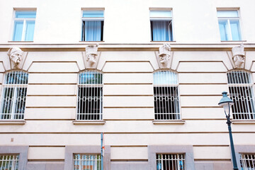 Vienna, Austria: building facade in the city center with carved stone soldier heads above barred windows, aligned in symmetry with vertical stripes and open windows above.