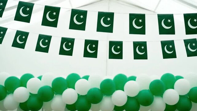 Rows of pakistan flags strung together above a festive arrangement of green and white balloons creating a celebratory atmosphere for a national event or holiday