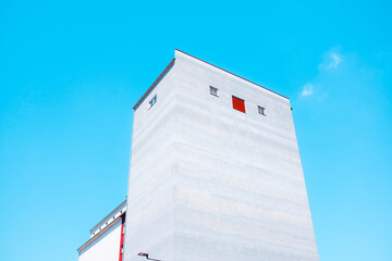Minimalist concrete building with flat gray walls, few windows, a single red door at the top. Concept for urban isolation, the 9-to-5 grind, and the psychological confinement of the modern rat race.