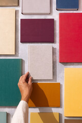 Hand picking a linen-covered book from a flat lay of colorful hardcovers on a textured background.