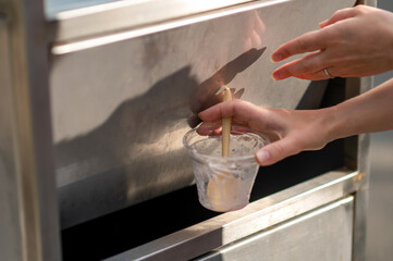 Female hands throwing empty plastic ice cream cup into trash bin outdoors
