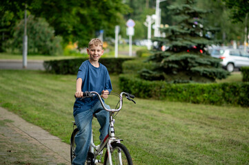 Happy blond teenage boy riding bicycle in sunny summer park, smiling and carefree
