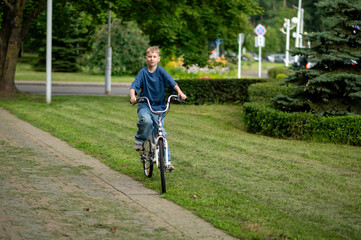 Happy blond teenage boy riding bicycle in sunny summer park, smiling and carefree