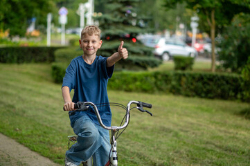 Smiling blond teen boy biking through green summer park on a sunny day