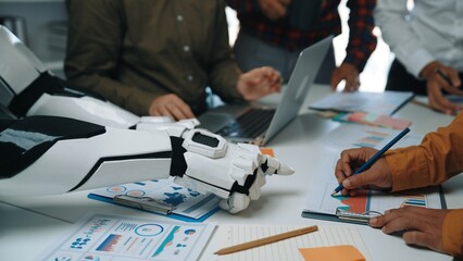 In a modern office setting, a robot arm collaborates with human participants during a meeting to analyze data, featuring charts and documents that showcase innovative strategies.Noogenesis