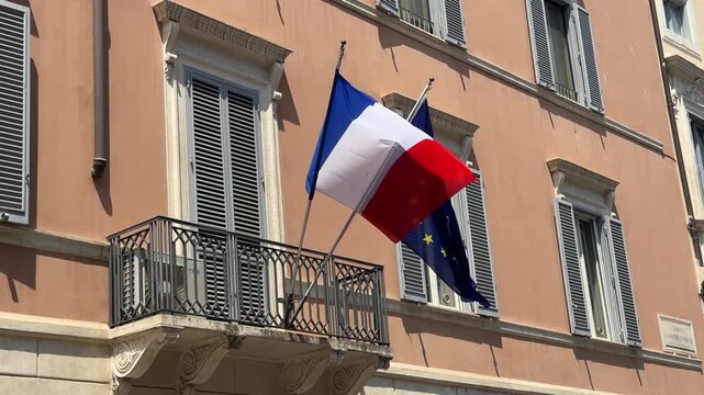 France and the EU flag on a flagpole of excellent quality. French Republic and the European Union waving flag with a building in the background.  