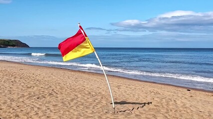 RNLI safety flag flying in the breeze on the beach in Scarborough North Bay on a bright and sunny summer day. Pull back shot