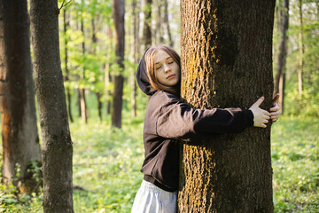 Teenage girl hugging tree, breathing fresh air and relieving stress in forest.