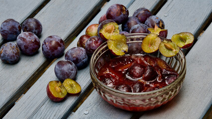 Pflaumenkompott auf einem grauen Holztisch. Pflaumen darum herum.