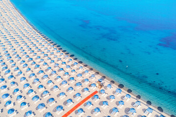 Aerial view of rows of beach umbrellas casting long shadows on the sand next to the crystal clear turquoise sea