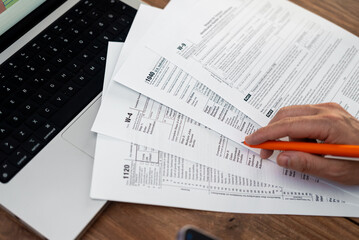 Male accountant consistently organizes financial records updating company data for filling tax forms covering various types of income at workplace with modern laptop