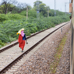 A woman dressed in colorful garments walks along the train on the railway