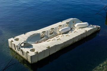 An empty modular plastic floating dock with white fenders moored on calm blue water, awaiting boats or swimmers, concept of marine infrastructure, boating, water recreation, modern marina equipment.
