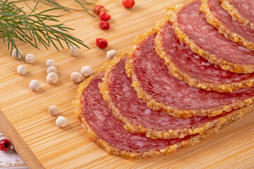 Artfully crued sliced servelat sausage garnished with spices on wood surface