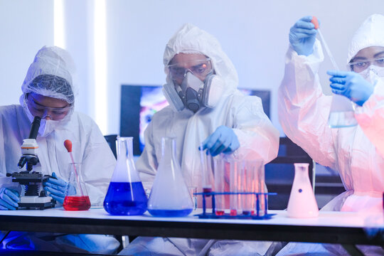 A team of chemists in hazmat suits discusses a breakthrough during a critical experiment in a secure lab. Concept for drug discovery and chemical research.