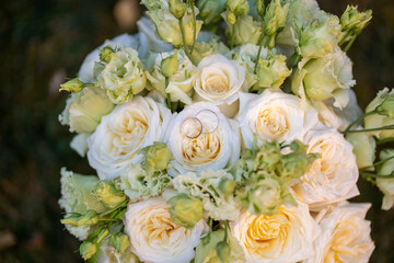 Elegant wedding bouquet of soft ivory and pastel peach roses with delicate green buds. Two gold wedding rings rest on the center rose, symbolizing love and commitment. Perfect for wedding invitations
