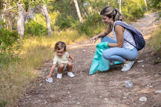 Toddler picking up litter from forest ground during cleanup