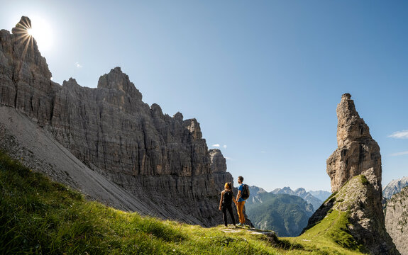 Iconic friulan mountain Campanile Di Val Montanaia, Dolomiti Friulane, Val Cimoliana, Cimolais Friuli Venezia Giulia, Italy. Two hikers stand on a grassy ledge, admiring the dramatic mountain scenery.