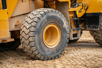 Obraz premium Heavy construction machinery tire on sandy ground at worksite showing rugged tread used in earthmoving operations and infrastructure construction environments