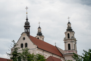 Obraz premium Historic baroque church with red roof and ornate towers under cloudy sky in Vilnius old town, Lithuania capital city, symbol of cultural heritage and religious architecture