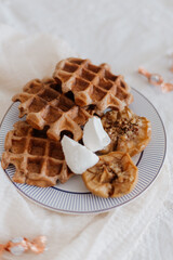 Waffles with baked apples and ricotta on porcelain plate, on white tablecloth with small candies, delicious breakfast, dessert, vertical image