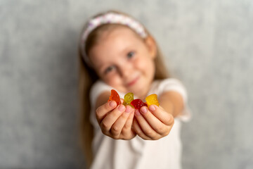 Vitamins for  kid. Little happy girl holding vitamins in the form of jelly bears. Soft focus on the face. Multivitamins in jelly.