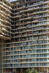 A multi-story building with balconies is under active construction, surrounded by scaffolding and equipment. The architectural structure showcases the scale of the project and urban development.