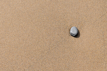 A single smooth grey stone placed on fine textured golden sand, photographed from above with ample negative space